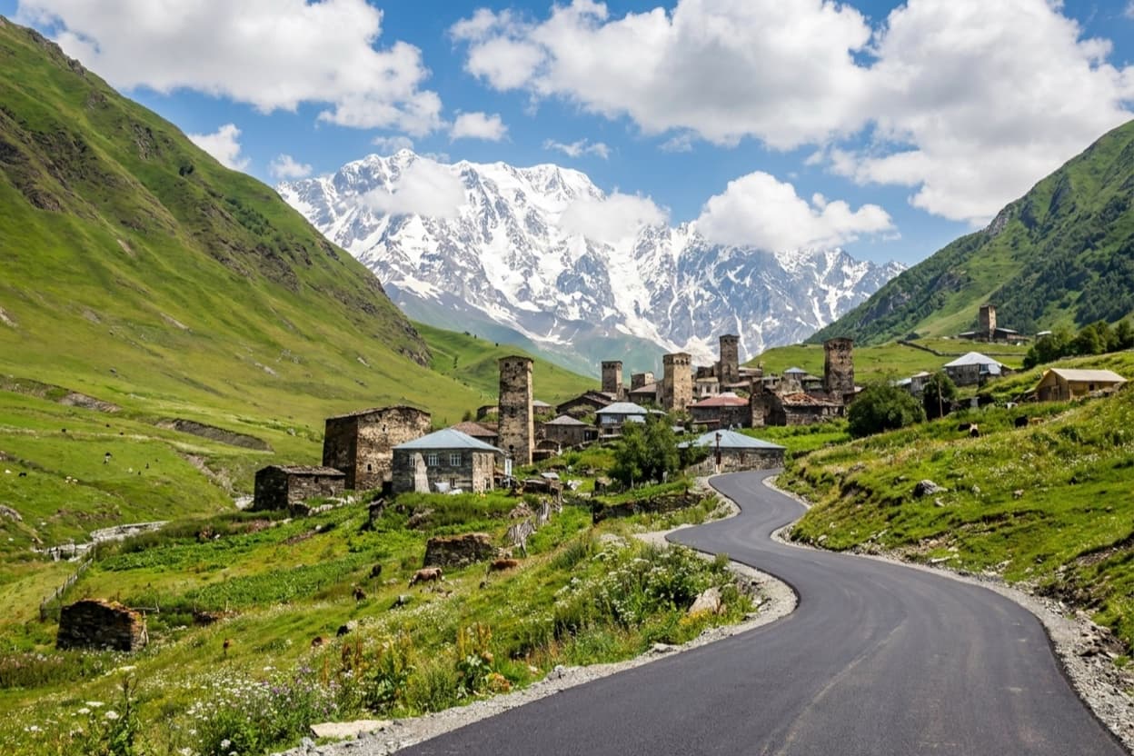 Medieval Svan towers of Ushguli village with the paved road curving toward it and Mount Shkhara behind
