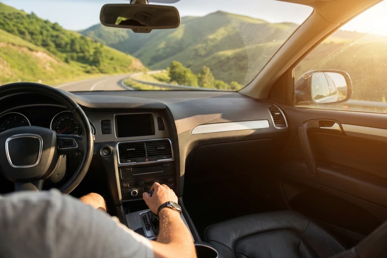 A driver's hand on the automatic gear selector of an SUV, mountain road visible through the windscreen